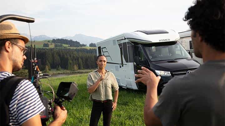 Woman filmed by a film crew in front of a motorhome